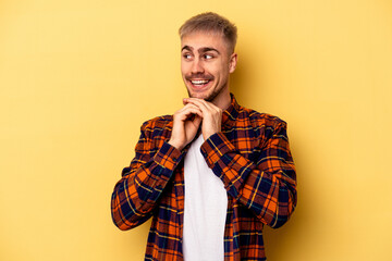 Young caucasian man isolated on yellow background praying for luck, amazed and opening mouth looking to front.