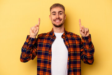 Young caucasian man isolated on yellow background indicates with both fore fingers up showing a...