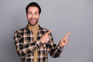 Photo of cute charming man wear plaid shirt pointing two fingers empty space isolated grey color background