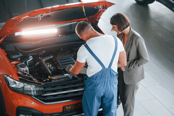 Woman in stylish clothes. Man repairing woman's automobile indoors. Professional service