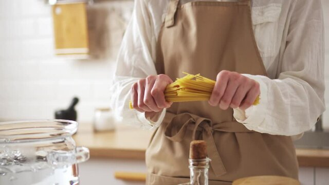 Hands breaking spaghetti pasta, cooking spaghetti in glass pan. macaroni break in hands fly at the waterfall saucepan water boiling water cook apron
