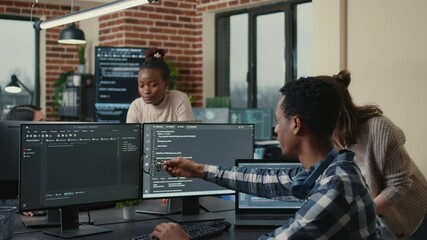 Programmer analyzing compiling code on multiple screens takes off glasses and doing high five hand gesture with colleague developer. Software developers celebrating successful coding.