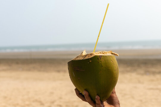 Tropical fresh coconut cocktail in female hand on white Tajpur beach, India.