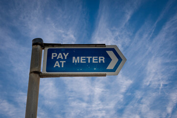 Blue pay at meter sign against a blue sky backround.