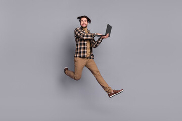 Photo of pretty funny guy dressed checkered shirt jumping high working modern device isolated grey color background