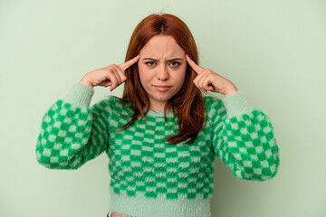 Young caucasian woman isolated on green background focused on a task, keeping forefingers pointing head.