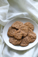Plate of healthy, gluten free and high protein cookies, made with bananas, eggs, chia seeds and almonds. White tablecloth and wooden background. Selective focus.