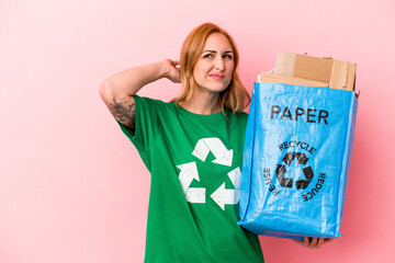 Young caucasian woman recycled paper isolated on pink background touching back of head, thinking...