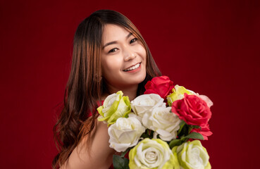 Beautiful young Asian woman smiling with a bouquet of red roses on red background.