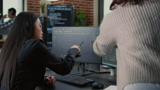 Programer pointing pencil at computer screen with software compiling code explaining source algorithm to coworker standing next to desk. Programmers discussing artificial intelligence with team.