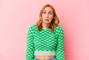 Young caucasian woman isolated on pink background shrugs shoulders and open eyes confused.