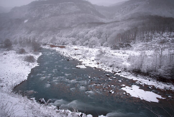 the Kuban mountain river at the mouth of the mountain slopes of Karachay-Cherkessia in winter with a snow-covered valley