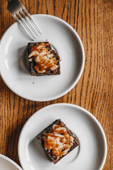 Two brownies on white plates on a wooden table shot from above.