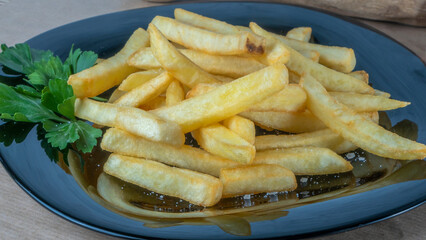 French fries on black dish on parchment background. Tasty golden french fries on a plate.
