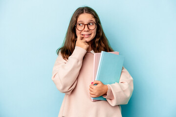 Little caucasian student girl holding books isolated on blue background biting fingernails, nervous...
