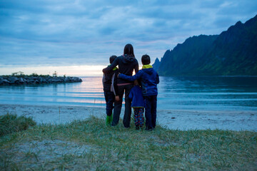 Fototapeta premium Children, enjoying sunset on Ersfjord Beach on Senja island, beautiful landscape view over the mountains