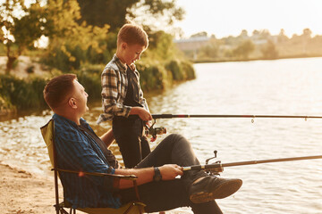 Sunny weather. Father and son on fishing together outdoors at summertime