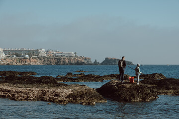 Father and son fishing in a rocky area of ​​Cabo de Palos in Spain on a cloudy winter day