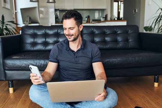 Handsome man working at home using smartphone and laptop