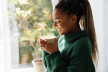 Young black woman with pigtails smiling while drinking tea