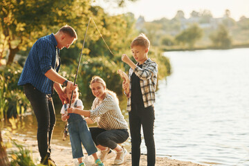 At summertime. Father and mother with son and daughter on fishing together outdoors
