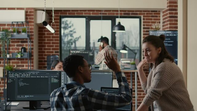 Two software developers doing high five hand gesture at desk with multiple screens running ai code celebrating successful algorithm. Programmers colleagues enjoying teamwork results in it agency.