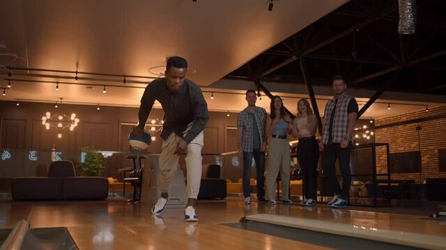 Multi ethnic Group of friends in a bowling club a black man throws a ball and knocks out a strike