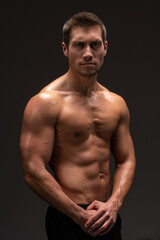 Fototapeta na wymiar Vertical shot of the handsome muscular guy posing isolated on black background, while showing his strong body and muscles
