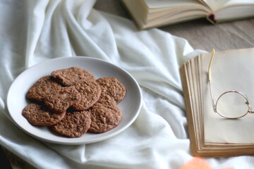 Lit candle, open books, reading glasses and plate of gluten free cookies on the table. Hygge at home. Selective focus.