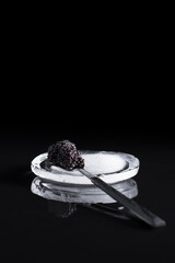 Caviar negro de esturión en una cuchara, sobre una piedra de hielo reflejada en fondo negro....