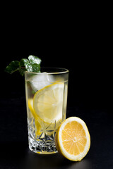 Un vaso de refrescante limonada, cóctel de frutas con rodajas de limón y hielo sobre fondo negro