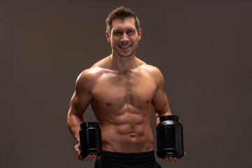 Waist up portrait view of the muscular bodybuilder holding two packs of protein powder and showing...