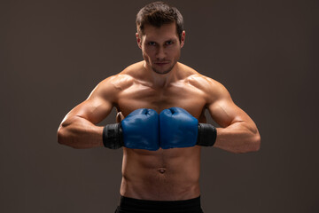 Boxing stance. Muscular caucasian sports man in gloves looking at camera over the brown studio...