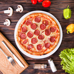 Meat pizza with sausages and cheese lies on a white plate on a wooden table