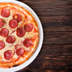 Meat pizza with sausages and cheese lies on a white plate on a wooden table
