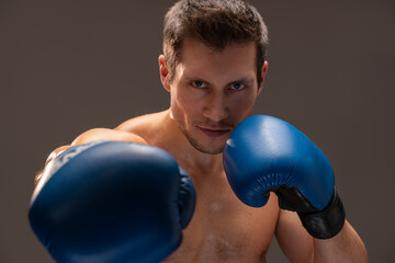 Boxing stance. Muscular caucasian sports man in gloves looking at camera over the brown studio...
