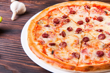 Meat pizza with sausages and cheese lies on a white plate on a wooden table