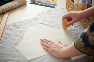 Closeup image of tailor marking out cardboard sewing pattern of short sleeve on grey fabric