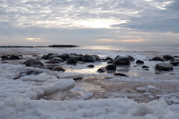 Ice blocks at the beach in winter evening by the sea with rocks
