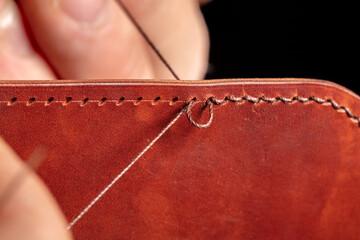 The hands of the master sew leather goods.