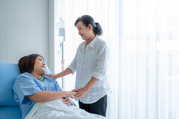 Obraz premium Asian woman, sick, stay in hospital. lying on the patient's bed beside the window Have a mother or an elderly woman come to visit and encourage