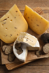 Board with delicious cheeses and fresh black truffles on wooden table, top view