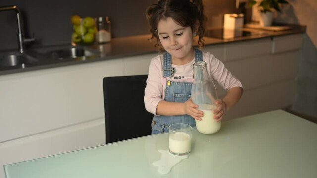 Little girl spills milk when she puts it in a crystal glass to drink it.Concept accidents at home children.