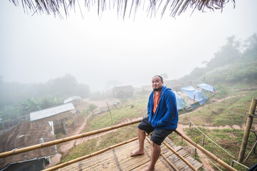 Asian fat traveler sitting on the wooden balcony with beautiful landscape and mist in the morning of Sapan Village nan Thailand.Sapan is Small and tranquil Village in the mountain.