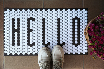 Stylish door mat with word Hello, shoes and beautiful flowers, flat lay