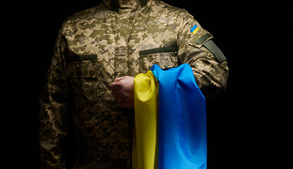 a soldier of the Ukrainian armed forces stands with a blue-yellow flag of Ukraine on a black...
