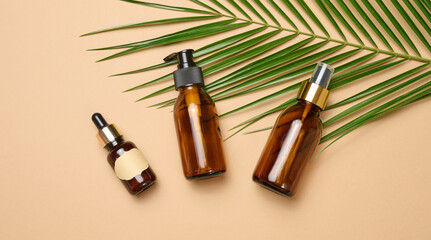 glass brown cosmetic bottles with pipette, spray and dispenser on brown background, top view. Containers for liquid products