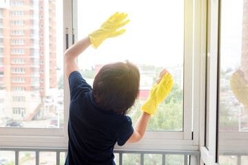 A small woman with difficulty washes the high windows  balcony.