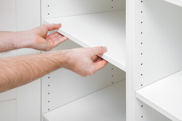 Young adult man hands putting shelf in white wardrobe. Assembling new wooden furniture. Closeup.