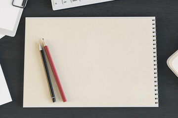 Top view of blank spiral notepad on dark wooden desktop with keyboard and pencils. Drawing, workplace, supplies and art concept. Mock up, 3D Rendering.